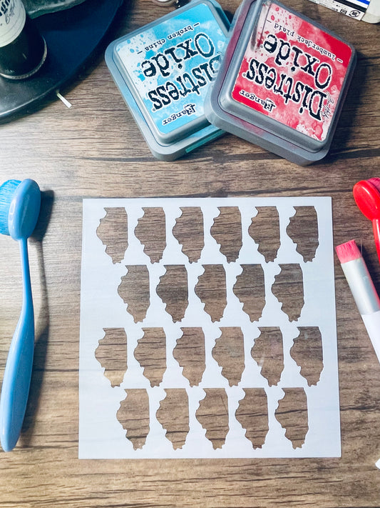 A sheet of white stencil paper with twenty irregular cutout shapes, displayed on a wooden table alongside craft tools and two Distress Oxide ink pads.
