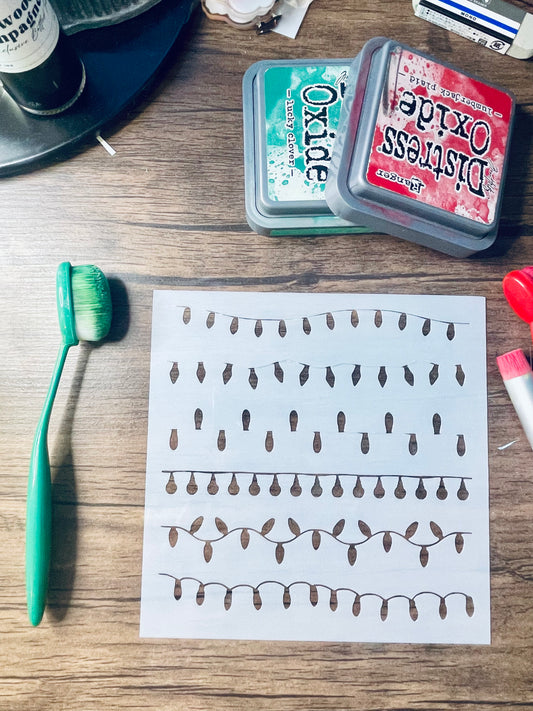 A printed sheet with rows of small brown teardrop-like shapes on white paper, placed on a wooden surface with a green toothbrush, two Distress Oxide ink pads, and other craft supplies nearby.