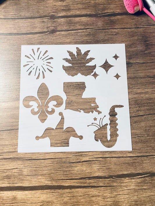 5.75” x 5.75” frosted stencil with Silhouettes of: a firework, Mardi Gras mask, sparkles, a fleur de lis, the shape of the state of Louisiana, a saxophone, and a jesters hat  .  Stencil is on a wood surface with a pink brush 