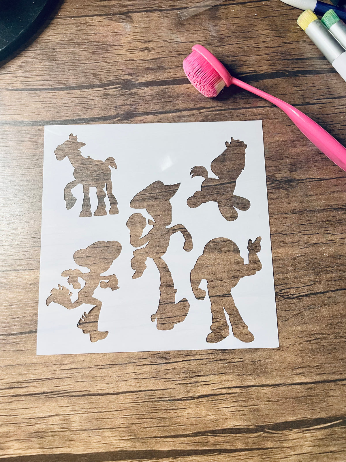 5.75” x 5.75” frosted stencil with five toy silhouettes including a cowboy running (twice), a space ranger waving, a plush unicorn and a toy horse. 