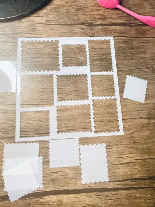 5.75” x 5.75” frosted stencil with Silhouettes of: 9 different stamp shaped cutouts.  The cutout pieces are on the edge of the stencil scattered around.  Stencil is on a wood surface with a pink brush 