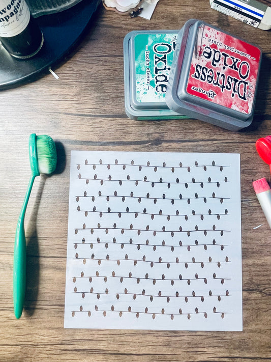 A printed sheet with rows of small black teardrop-like marks on a white background, placed on a wooden tabletop alongside a green toothbrush, two Distress Oxide ink pads, and other craft supplies.