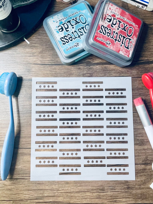 A sheet of craft transfer stickers featuring horizontal brown bars with star patterns, displayed on a wooden table alongside stamping tools and Distress Oxide ink pads.