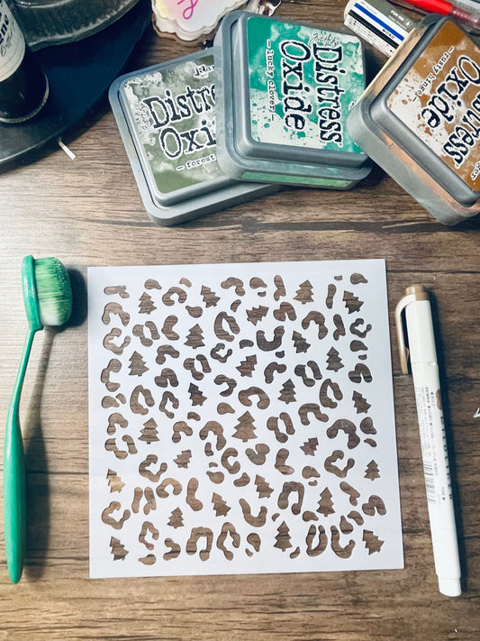 A sheet of leopard print stencils or decals displayed on a wooden table, surrounded by craft supplies including Distress Oxi ink pads, a green toothbrush, and a white marker.