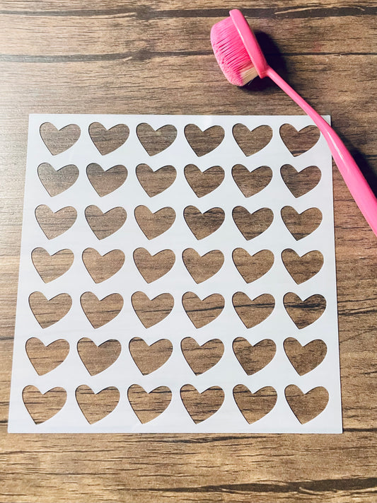 5.75” x 5.75” frosted stencil with Silhouettes of: full hearts in linear pattern down the stencil.  Stencil is on a wood surface with a pink brush 