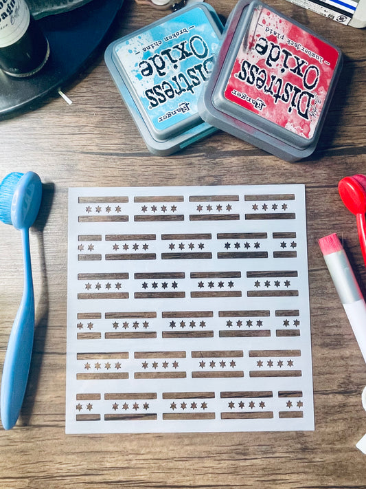 A sheet of nail wraps or stickers with horizontal brown bars and star motifs, displayed on a wooden table alongside Distress Oxide ink pads, a blue brush, and other craft tools.