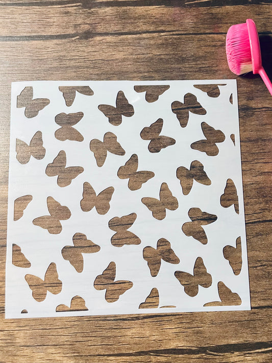 5.75” x 5.75” frosted stencil with Silhouettes of: multiple butterfly silhouettes flying around in a random pattern.  Stencil is on a wood surface with a pink brush 