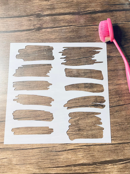 5.75” x 5.75” frosted stencil with Silhouettes of: 11 different styles of brush stroke stencils.  Stencil is on a wood surface with a pink brush 