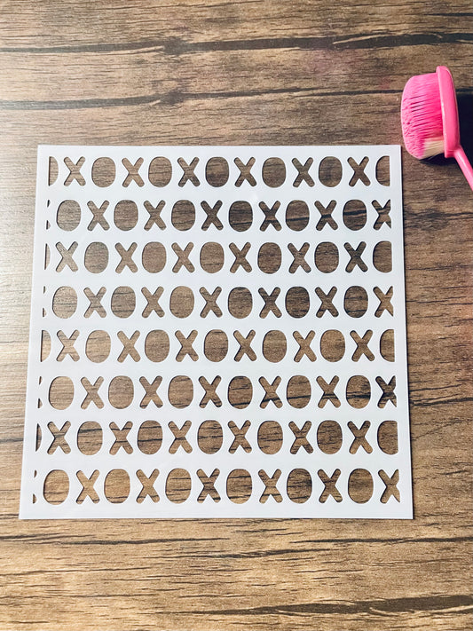 5.75” x 5.75” frosted stencil with Silhouettes of: repeating horizontal lines of xoxoxo.  Stencil is on a wood surface with a pink brush 