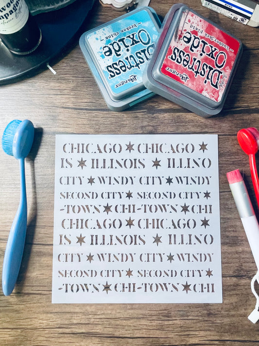 A sheet of metal stencils with Chicago-themed text and star motifs is displayed on a wooden table, surrounded by craft tools and Distress Oxide ink pads.